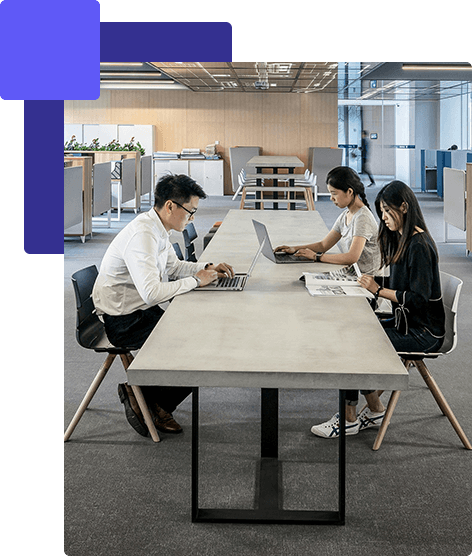 三個人在現代辦公空間的長桌旁工作,使用筆記型電腦並閱讀印刷資料,他們合作進行創新的香港 AI 專案。. 香港AI